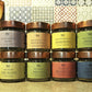 8 aromi in barattolo di vetro con etichette colorate e tappi color rame con sfondo piastrelle cucina attrezzi in legno 